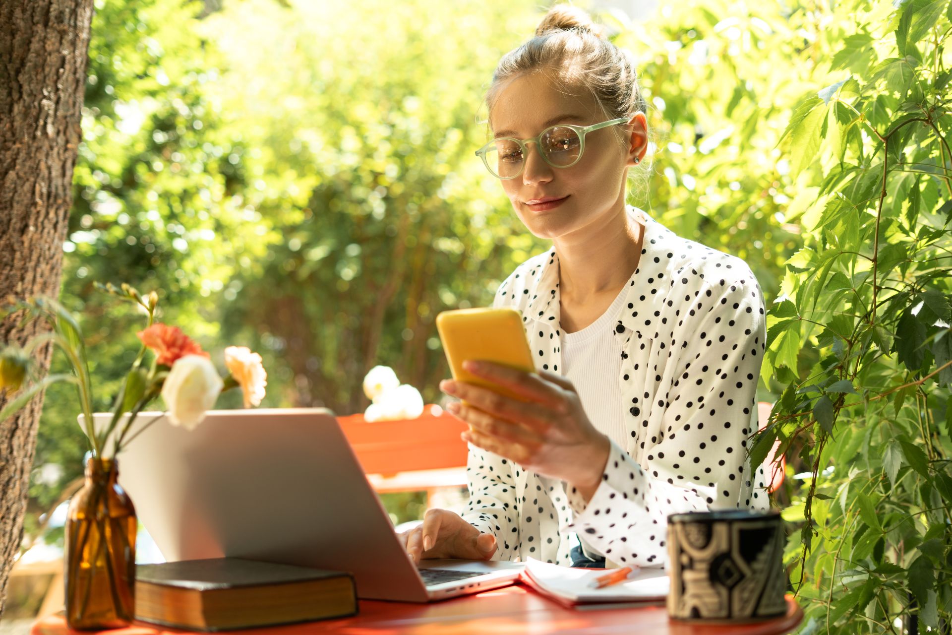 Frau arbeitet am Laptop und nutzt Smartphone im Garten