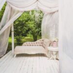 Gemuetlicher Holzpavillon mit weißen Vorhängen und rustikalem Sitzbereich im Garten